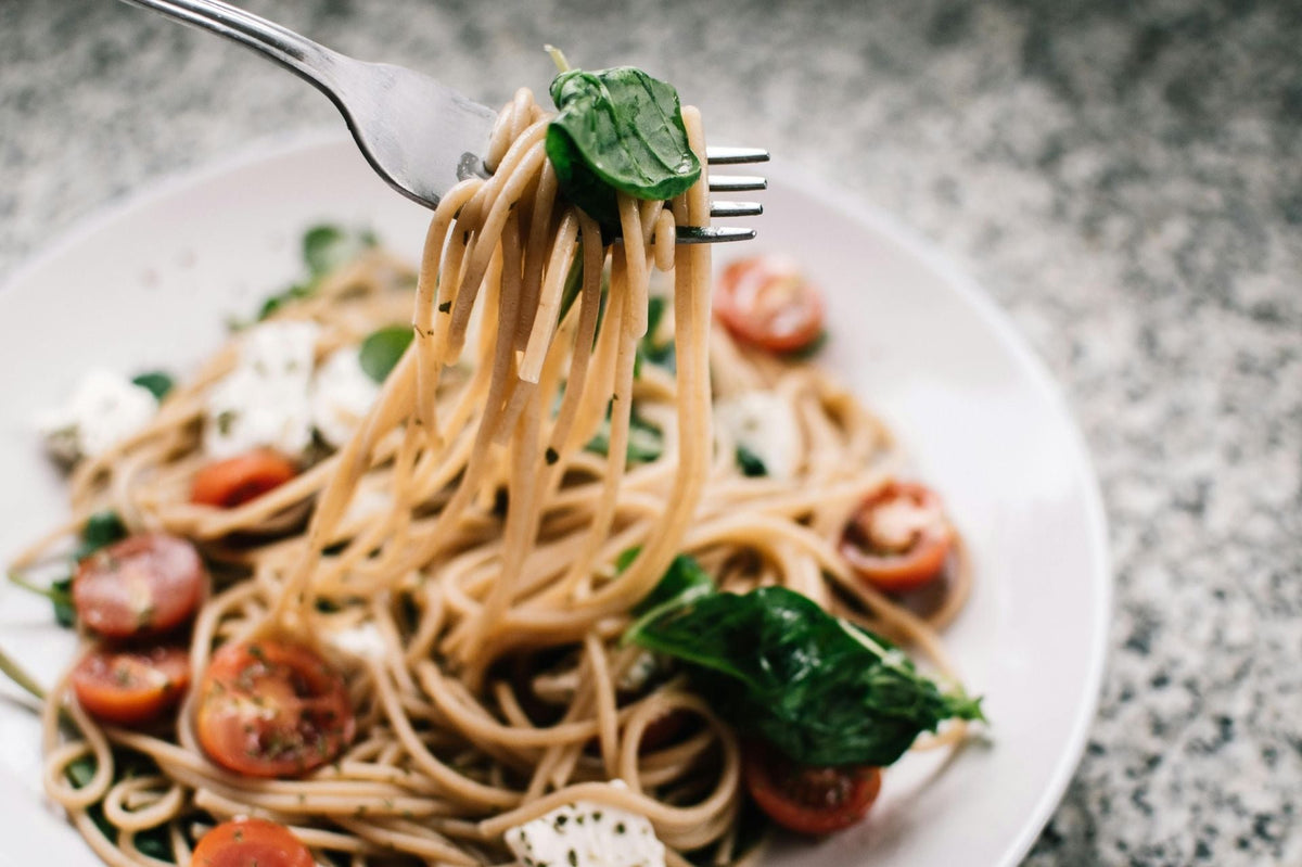 Prato de macarrão sem glúten servido com tomates, folhas verdes e molho leve, destacando massa caseira e alimentação sem glúten.