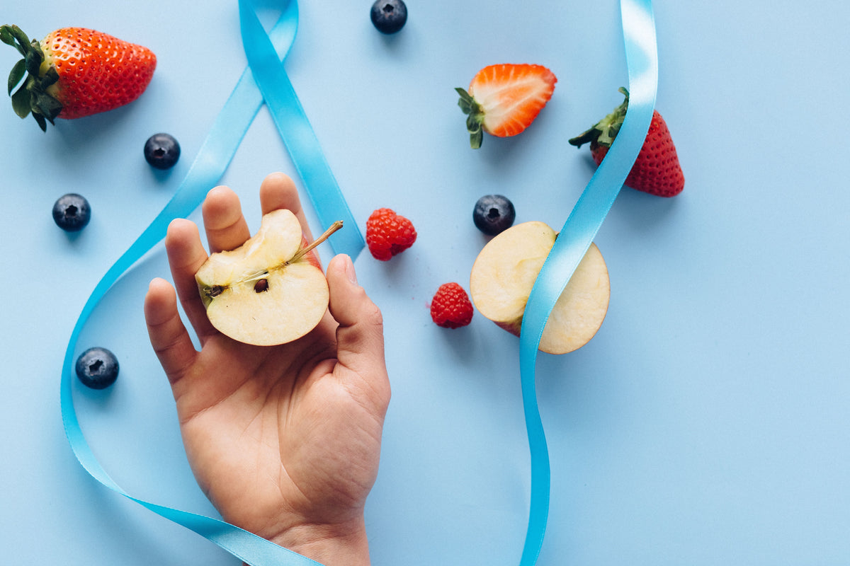 frutas como morango maça mirtilo e framboesa em cima de uma superficie azul com uma fita azul passando entre elas