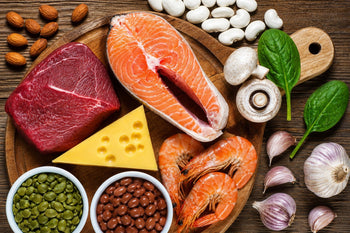 Alimentos ricos em zinco como carne vermelha, salmão, camarão, queijo, sementes de abóbora, feijão, castanhas, cogumelos e espinafre sobre mesa de madeira